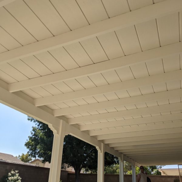 A freshly painted backyard patio cover in Santa Clarita, featuring a clean white finish on all beams and rafters, providing a bright outdoor living space by Paint Daddy.