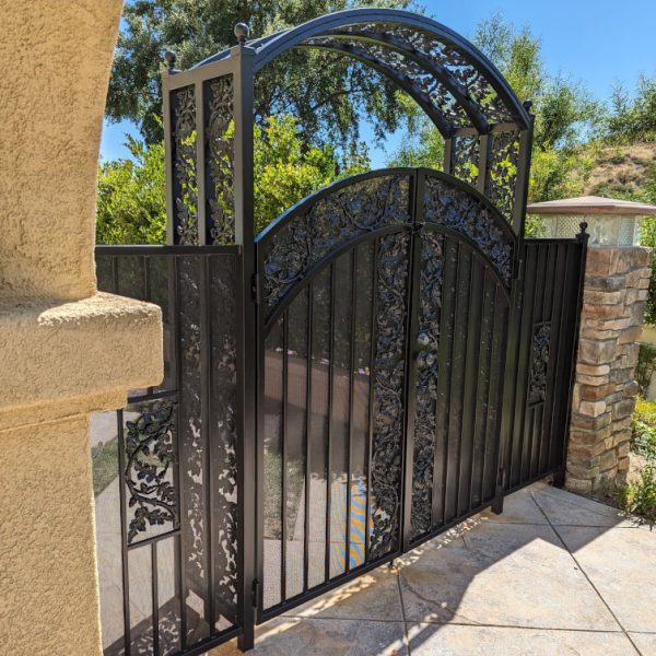 A custom ornamental wrought iron gate with an intricate arched header, recently painted with a durable semigloss black finish, completed by Paint Daddy in Santa Clarita.